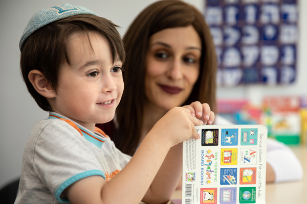Young child and mother learn together. He has book open, and she looks lovingly at him.